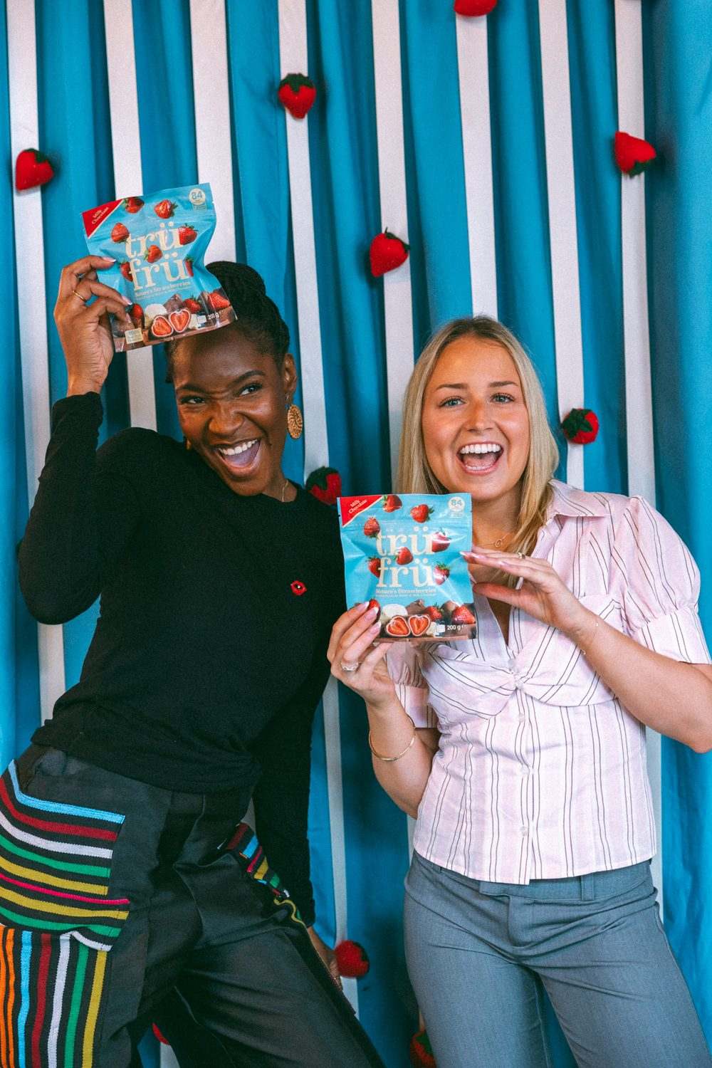 Two guests holding packs of Trü Frü at the strawberry photo wall.