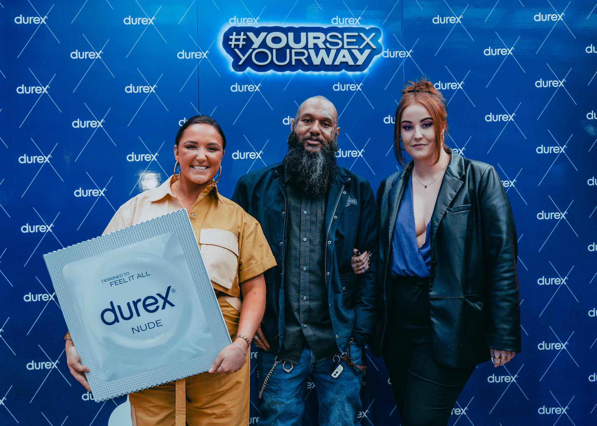 Guests at a Durex event, one holding an oversized condom pack, against a branded wall.