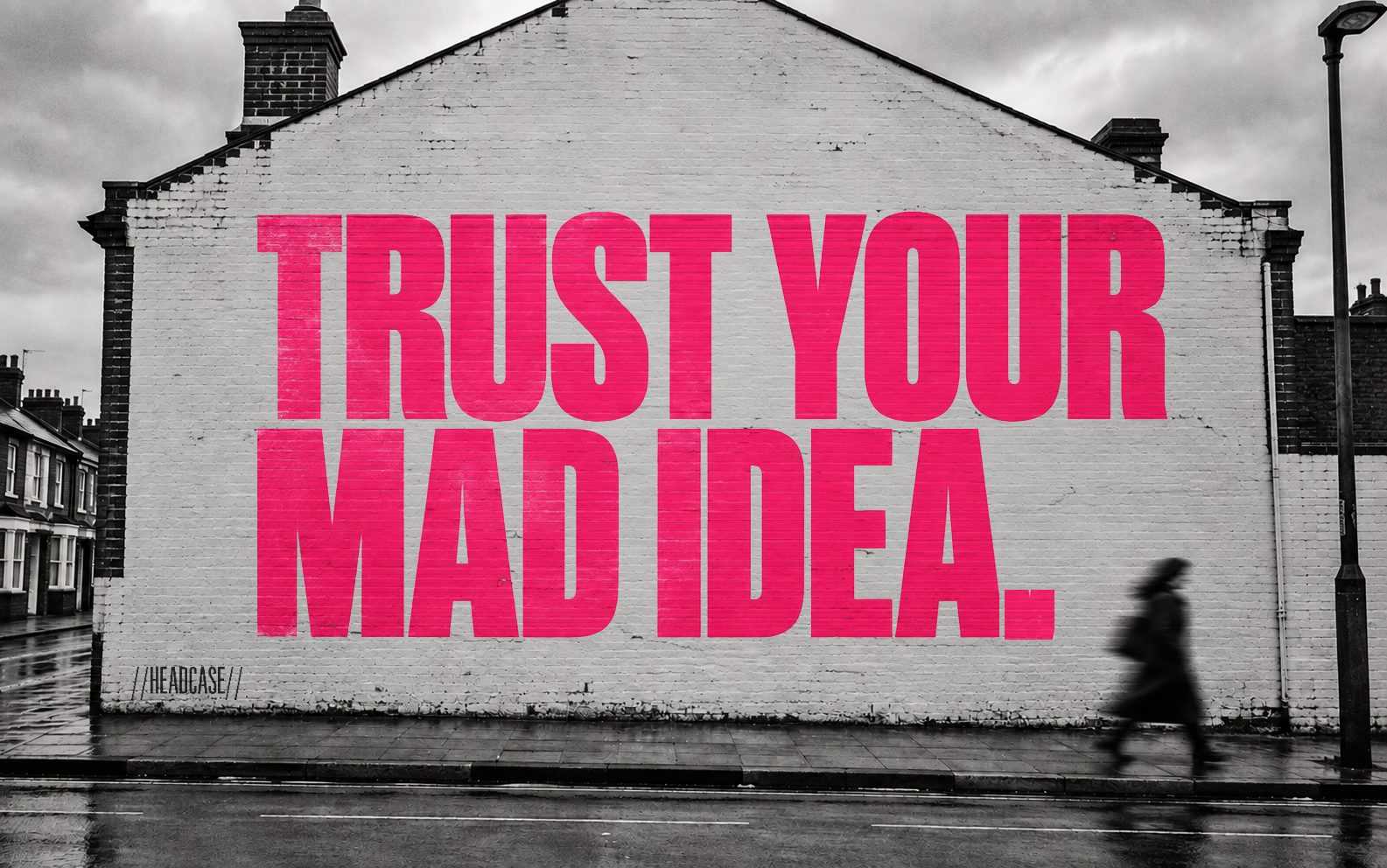 Trust your mad idea, painted across the gable wall of a terraced house, signed Headcase, a woman walking past.