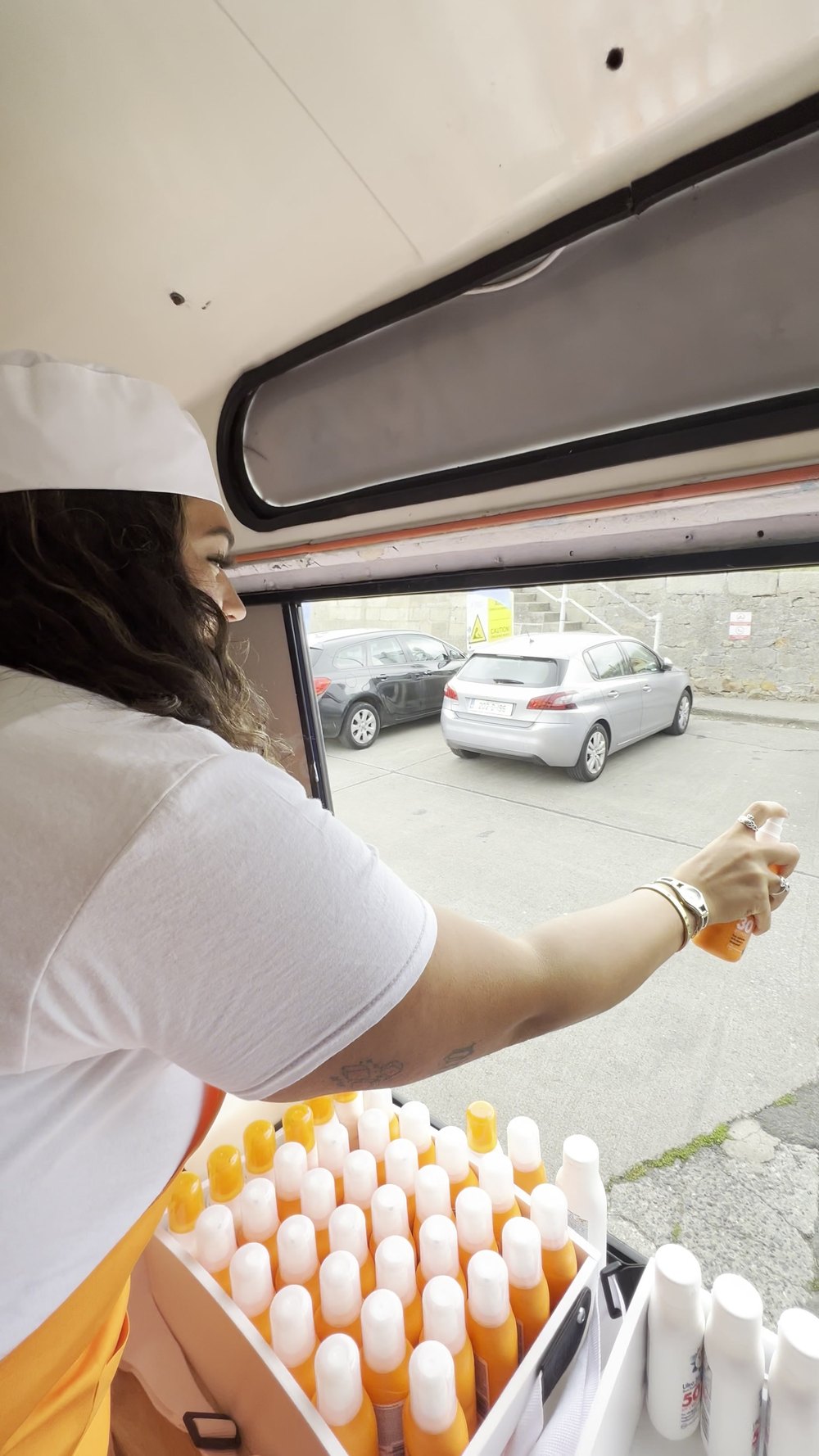 A brand ambassador reaching out through the serving hatch of the Sun Cream Van with a bottle of Cien.