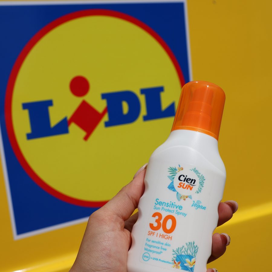 A hand holding a bottle of Cien Sun SPF30 against the Lidl logo on the side of the van.